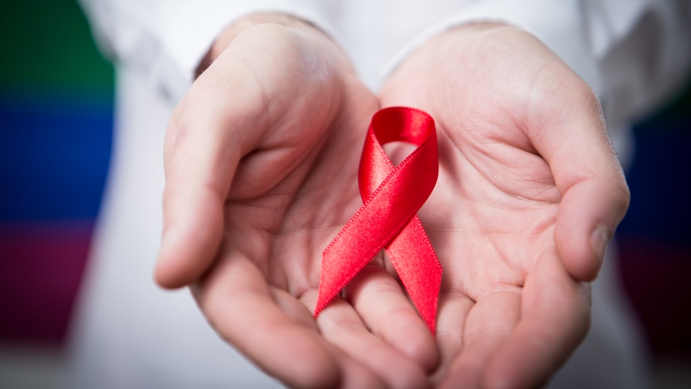 A person holds a red ribbon symbolizing awareness for HIV-AIDS. (wavebreakmedia/shutterstock.com)