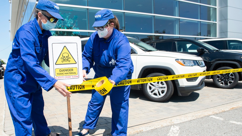 Members of the Quebec branch of Extinction Rebellion wrap caution tape around SUVs at a dealership to highlight the ongoing climate crisis in Montreal, Saturday, July 10, 2021. THE CANADIAN PRESS/Graham Hughes 