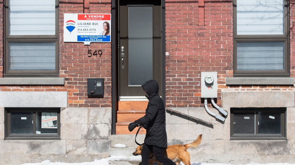 A woman walks by a house for sale in Montreal, Friday, March 4, 2022. THE CANADIAN PRESS/Graham Hughes