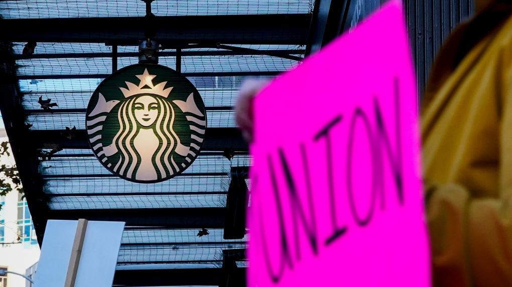 Cassandra Gonzalez holds a "union" sign while passing in front a Starbucks logo as workers participate in a walkout and strike during the company's Red Cup Day Thursday, Nov. 16, 2023, near Pike Place Market in Seattle. (AP Photo/Lindsey Wasson)